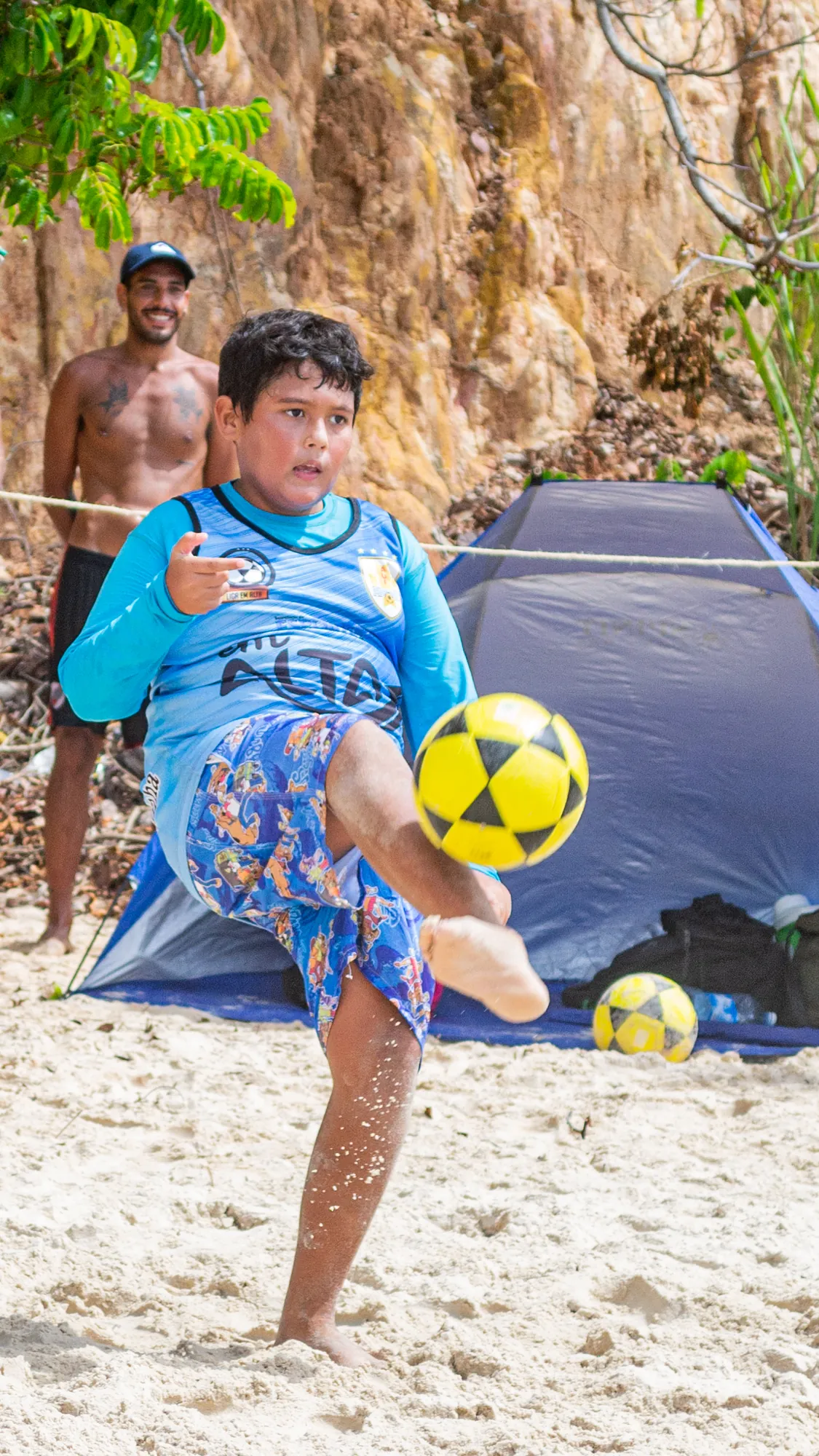 Criança chutando a bola de altinha na areia